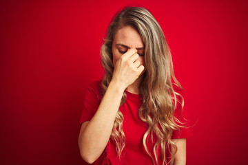 Young beautiful woman wearing basic t-shirt standing over red isolated background tired rubbing nose and eyes feeling fatigue and headache. Stress and frustration concept.