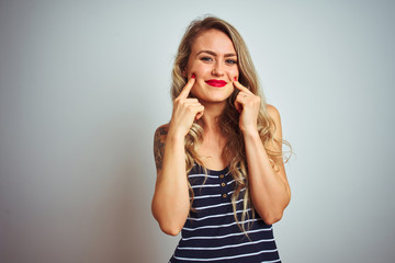 Fototapeta premium Young beautiful woman wearing stripes t-shirt standing over white isolated background Smiling with open mouth, fingers pointing and forcing cheerful smile