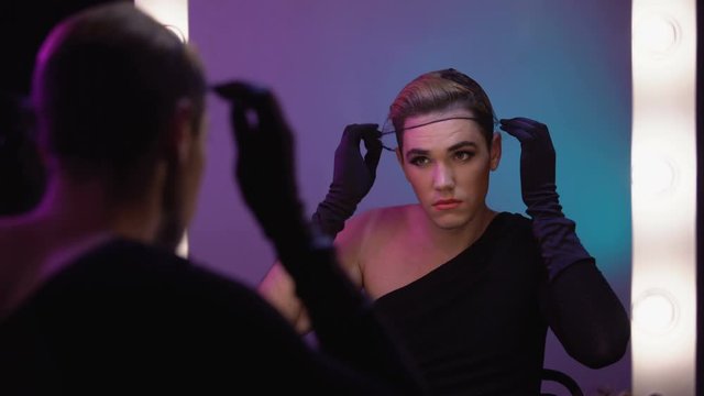 Beautiful drag queen putting on wig cap looking in mirror, cabaret celebrity