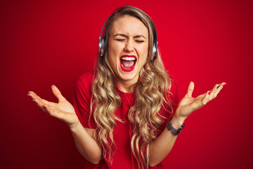 Fototapeta premium Young beautiful woman wearing headphones over red isolated background celebrating mad and crazy for success with arms raised and closed eyes screaming excited. Winner concept