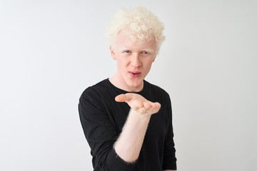 Young albino blond man wearing black t-shirt standing over isolated white background looking at the camera blowing a kiss with hand on air being lovely and sexy. Love expression.