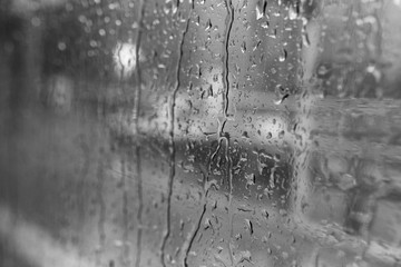 Black and white mood and tone, close up and macro view of raining water drop on outside windows of the bus or train white blur abstract street view.