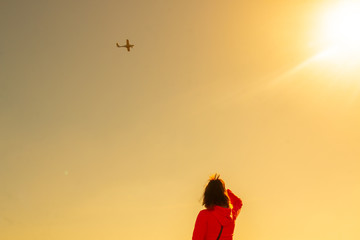 Woman watching a plane flying through the sky. Plane flying on sunset. Copy space for text.