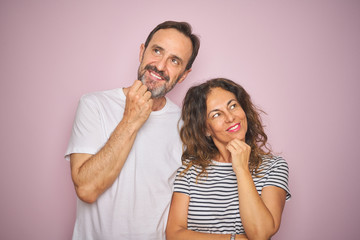 Beautiful middle age couple together standing over isolated pink background with hand on chin thinking about question, pensive expression. Smiling with thoughtful face. Doubt concept.