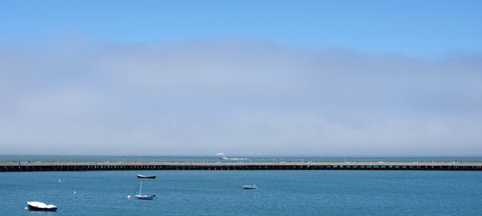 Panoramic view of the long public pier along the San Francisco marina with fog behind over Alcatraz...