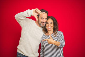 Beautiful middle age couple wearing winter sweater over isolated red background smiling making...