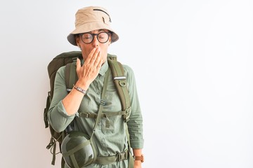 Middle age hiker woman wearing backpack canteen hat glasses over isolated white background bored yawning tired covering mouth with hand. Restless and sleepiness.