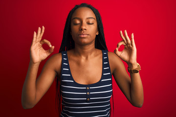 Young african american woman wearing striped t-shirt standing over isolated red background relax and smiling with eyes closed doing meditation gesture with fingers. Yoga concept.