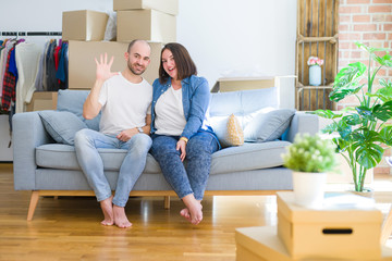 Young couple sitting on the sofa arround cardboard boxes moving to a new house showing and pointing up with fingers number five while smiling confident and happy.