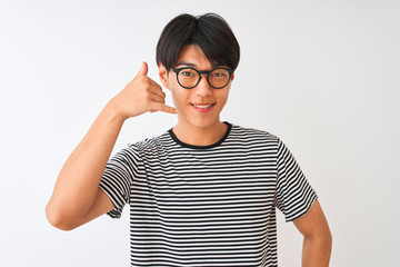 Chinese man wearing glasses and navy striped t-shirt standing over isolated white background smiling doing phone gesture with hand and fingers like talking on the telephone. Communicating concepts.