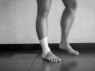 Black and white version of Athlete performing mobility exercises on injured ankle with a tape job