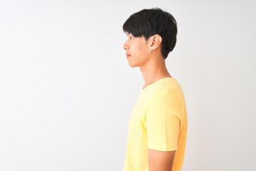 Chinese man wearing yellow casual t-shirt standing over isolated white background looking to side,...