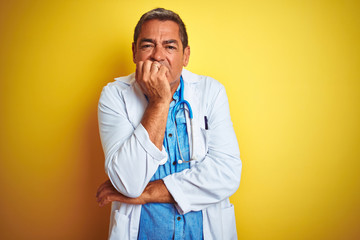 Handsome middle age doctor man wearing stethoscope over isolated yellow background looking stressed and nervous with hands on mouth biting nails. Anxiety problem.