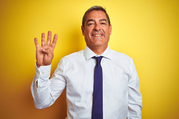 Handsome middle age businessman standing over isolated yellow background showing and pointing up with fingers number four while smiling confident and happy.
