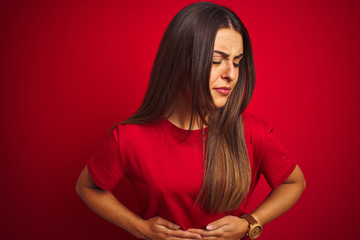 Young beautiful woman wearing t-shirt standing over isolated red background with hand on stomach...