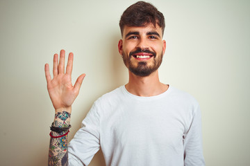 Young man with tattoo wearing t-shirt standing over isolated white background showing and pointing up with fingers number five while smiling confident and happy.