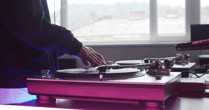 Close-up modern DJ mixer controller disc with neon illumination in recording studio. DJ hands touching sliders mixing sounds in slow motion.