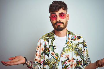 Man with tattoo on vacation wearing summer shirt sunglasses over isolated white background clueless...