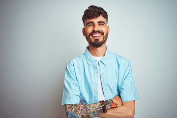 Young man with tattoo wearing blue shirt standing over isolated white background happy face smiling...