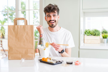 Young man eating asian sushi from home delivery screaming proud and celebrating victory and success very excited, cheering emotion