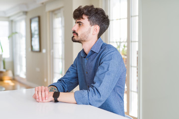 Naklejka na ściany i meble Young man wearing casual shirt sitting on white table looking to side, relax profile pose with natural face with confident smile.