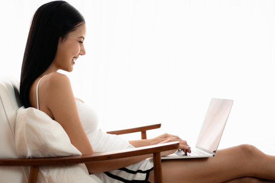 beautiful asian woman in casual wear sitting on arm chair using laptop computer in a cozy living room