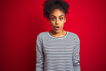Fototapeta na wymiar African american woman wearing navy striped t-shirt standing over isolated red background afraid and shocked with surprise expression, fear and excited face.