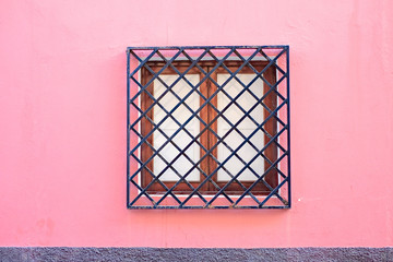 Barred squre window in a pale pink facade of an elegant European villa home.