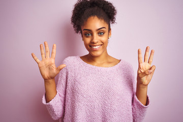 Young african american woman wearing winter sweater standing over isolated pink background showing and pointing up with fingers number eight while smiling confident and happy.