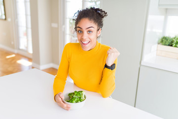 Young african american girl eating heatlhy green broccoli screaming proud and celebrating victory and success very excited, cheering emotion