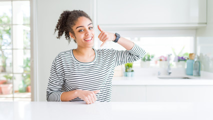 Beautiful african american woman with afro hair wearing casual striped sweater smiling doing phone gesture with hand and fingers like talking on the telephone. Communicating concepts.