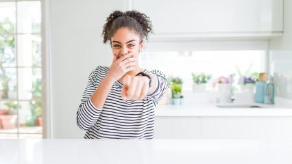 Beautiful african american woman with afro hair wearing casual striped sweater laughing at you, pointing finger to the camera with hand over mouth, shame expression