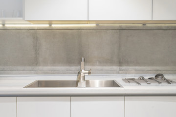 Detail of a white rectangular designer kitchen sink with chrome water tap against a tiled wall