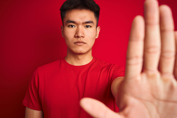 Naklejka premium Young asian chinese man wearing t-shirt standing over isolated red background with open hand doing stop sign with serious and confident expression, defense gesture