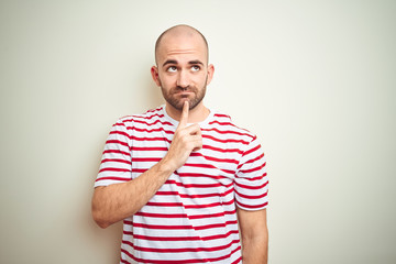 Young bald man with beard wearing casual striped red t-shirt over white isolated background Thinking concentrated about doubt with finger on chin and looking up wondering