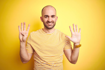 Young bald man with beard wearing casual striped t-shirt over yellow isolated background showing...