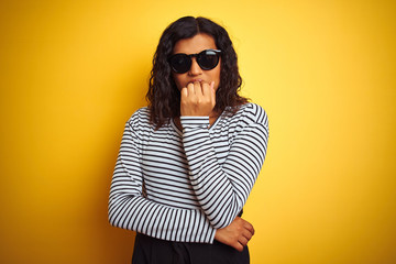 Transsexual transgender woman wearing sunglasses over isolated yellow background looking stressed and nervous with hands on mouth biting nails. Anxiety problem.