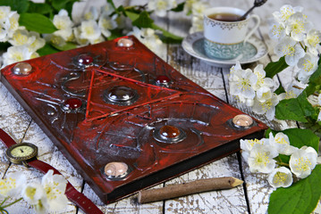 Magic book with decorated cover, old watches and cup on witch table.