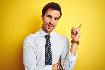 Young handsome businessman wearing elegant shirt and tie over isolated yellow background with a big smile on face, pointing with hand and finger to the side looking at the camera.