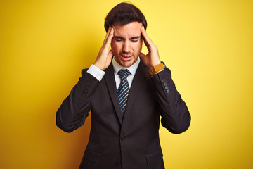 Young handsome businessman wearing suit and tie standing over isolated yellow background with hand on headache because stress. Suffering migraine.