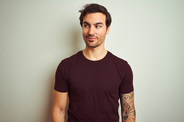 Young handsome man with tattoo wearing purple casual t-shirt over isolated white background smiling looking to the side and staring away thinking.