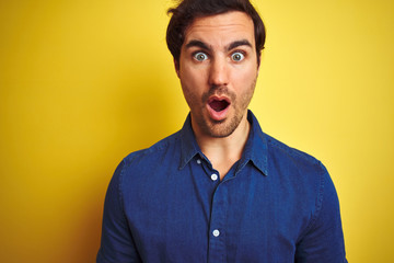 Fototapeta premium Young handsome man with tattoo wearing casual shirt standing over isolated yellow background scared in shock with a surprise face, afraid and excited with fear expression