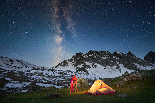 Couple standing near tent and looking at the milky way in mountains at night