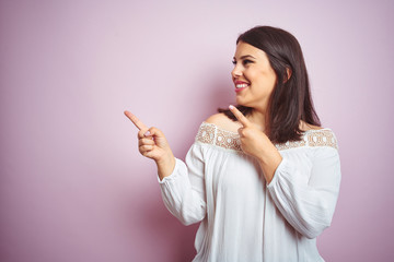 Young beautiful brunette woman over pink isolated background smiling and looking at the camera pointing with two hands and fingers to the side.