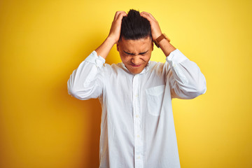 Young brazilian businessman wearing elegant shirt standing over isolated yellow background suffering from headache desperate and stressed because pain and migraine. Hands on head.