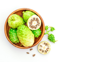 Fresh raw and ripe Morinda citrifolia or Noni fruit and sliced with seeds in wooden bowl isolated on white background.