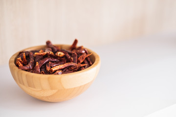Dry red chilli in a wooden bowl on a white shelf in natural light.
