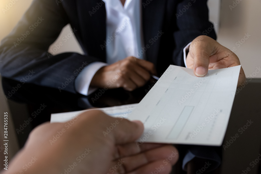 Wall mural Business woman or manager in suit hand holding pen and giving bank check to colleague with checkbook on the  desk at office. Payday and payment by cheque concept