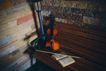 violin, bow and open book on a bench by the stone wall