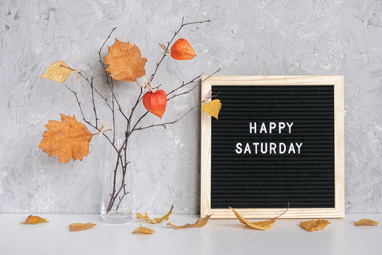 Happy Saturday text on black letter board and bouquet of branches with yellow leaves on clothespins in vase on table Template for postcard, greeting card Concept Hello autumn Saturday